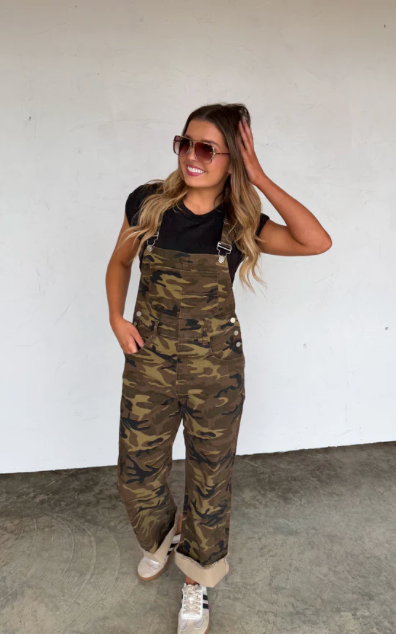 Woman wearing camouflage overalls against a white wall