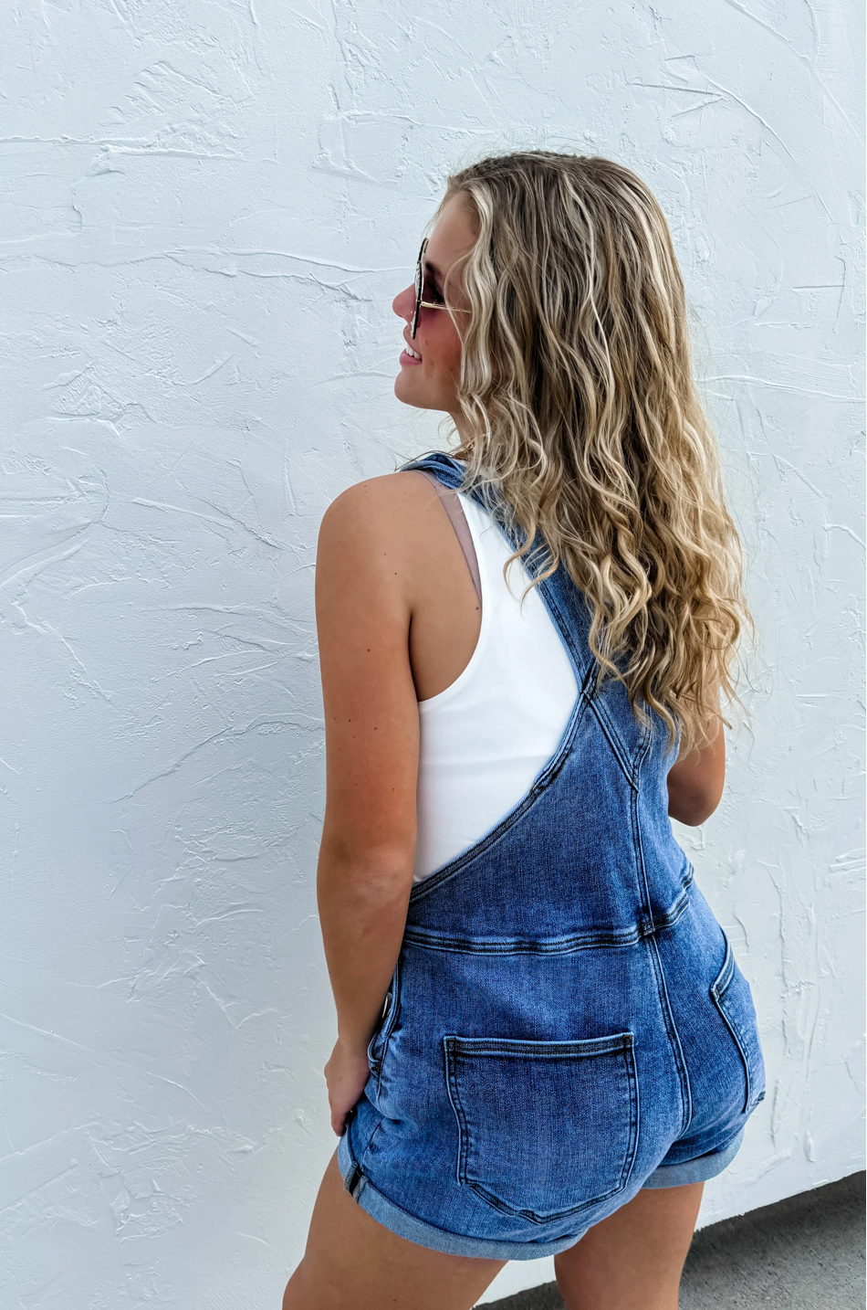 Woman wearing denim overalls against a white textured wall