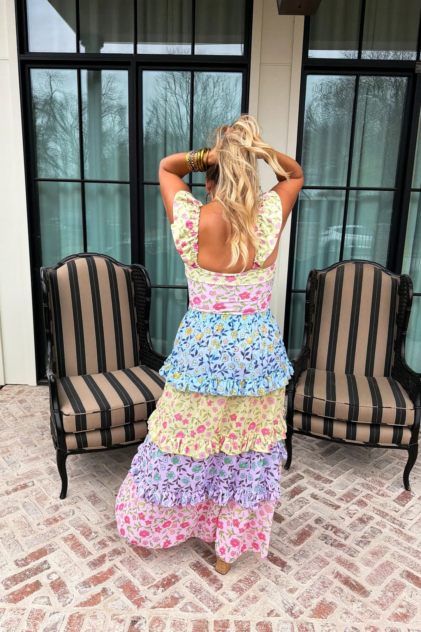 Woman in a colorful, layered dress standing in front of a glass door with striped chairs.