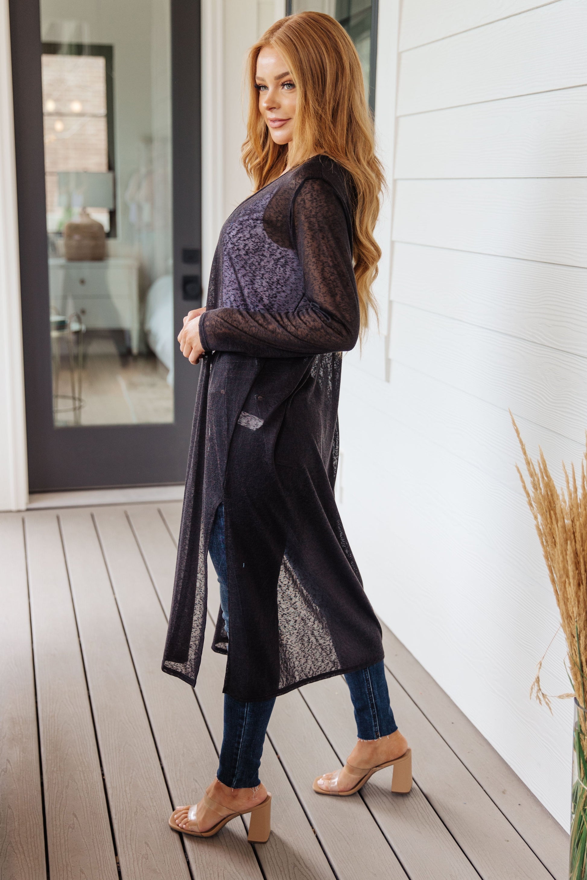Woman wearing a long dark cardigan on a wooden deck.