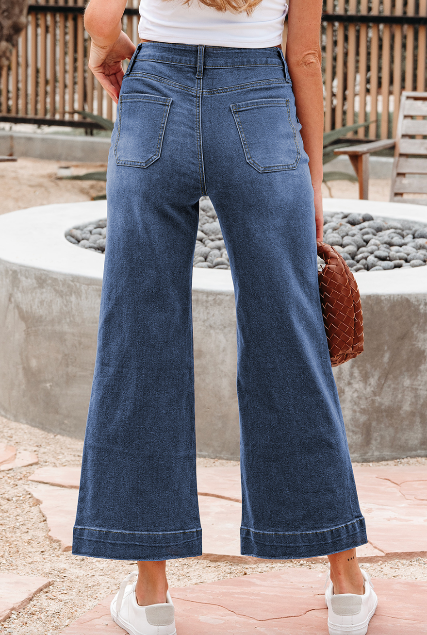 Person wearing blue jeans standing outdoors near a stone wall.