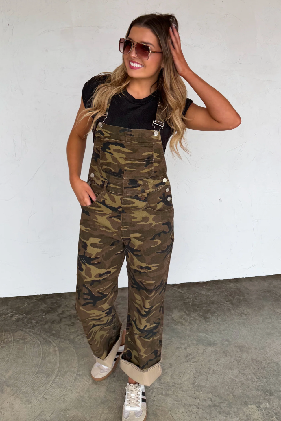 Woman wearing camouflage overalls against a white wall