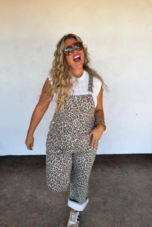 Woman wearing leopard print overalls and sunglasses against a white wall.
