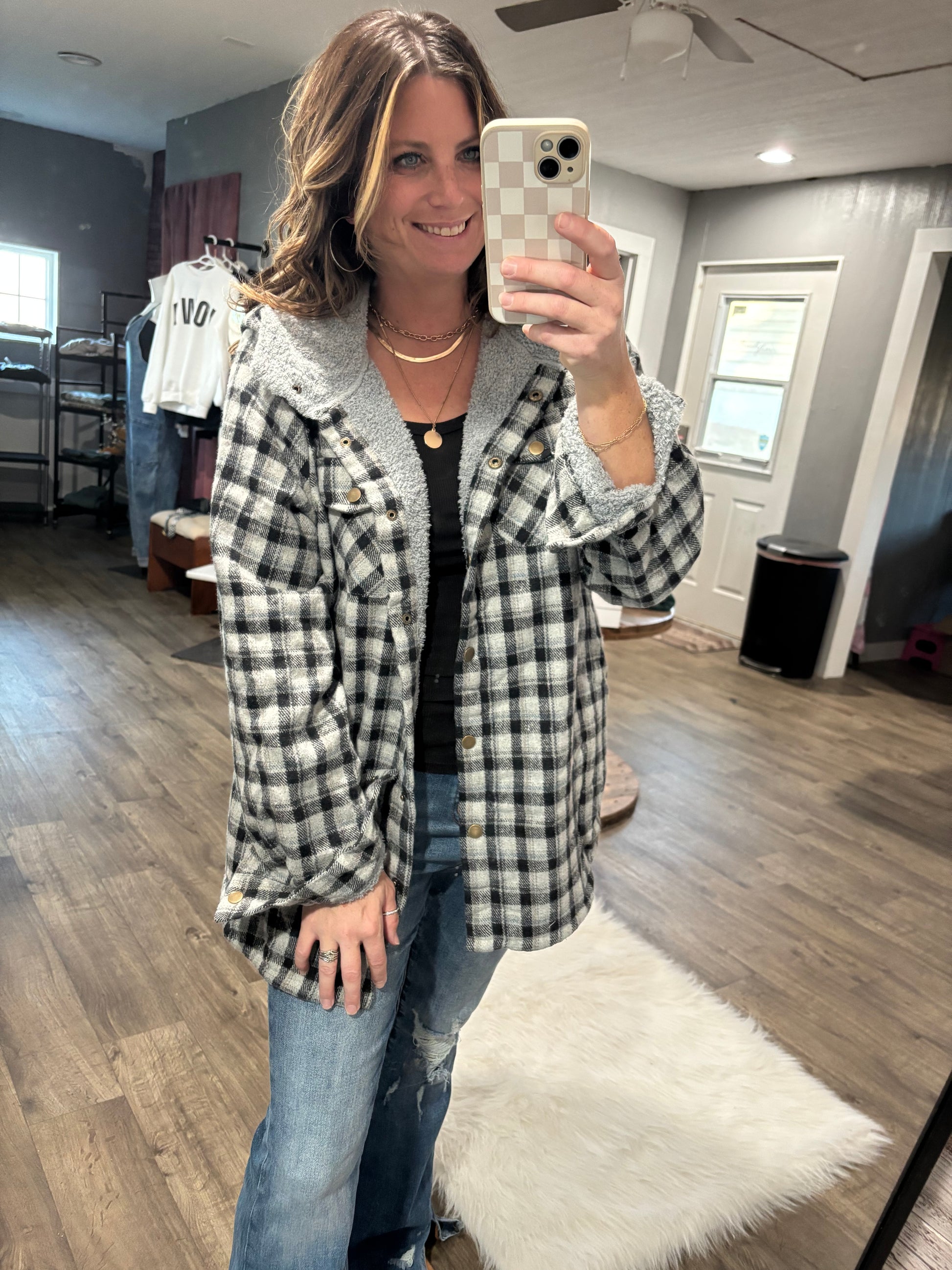 Person wearing a plaid coat taking a mirror selfie indoors.