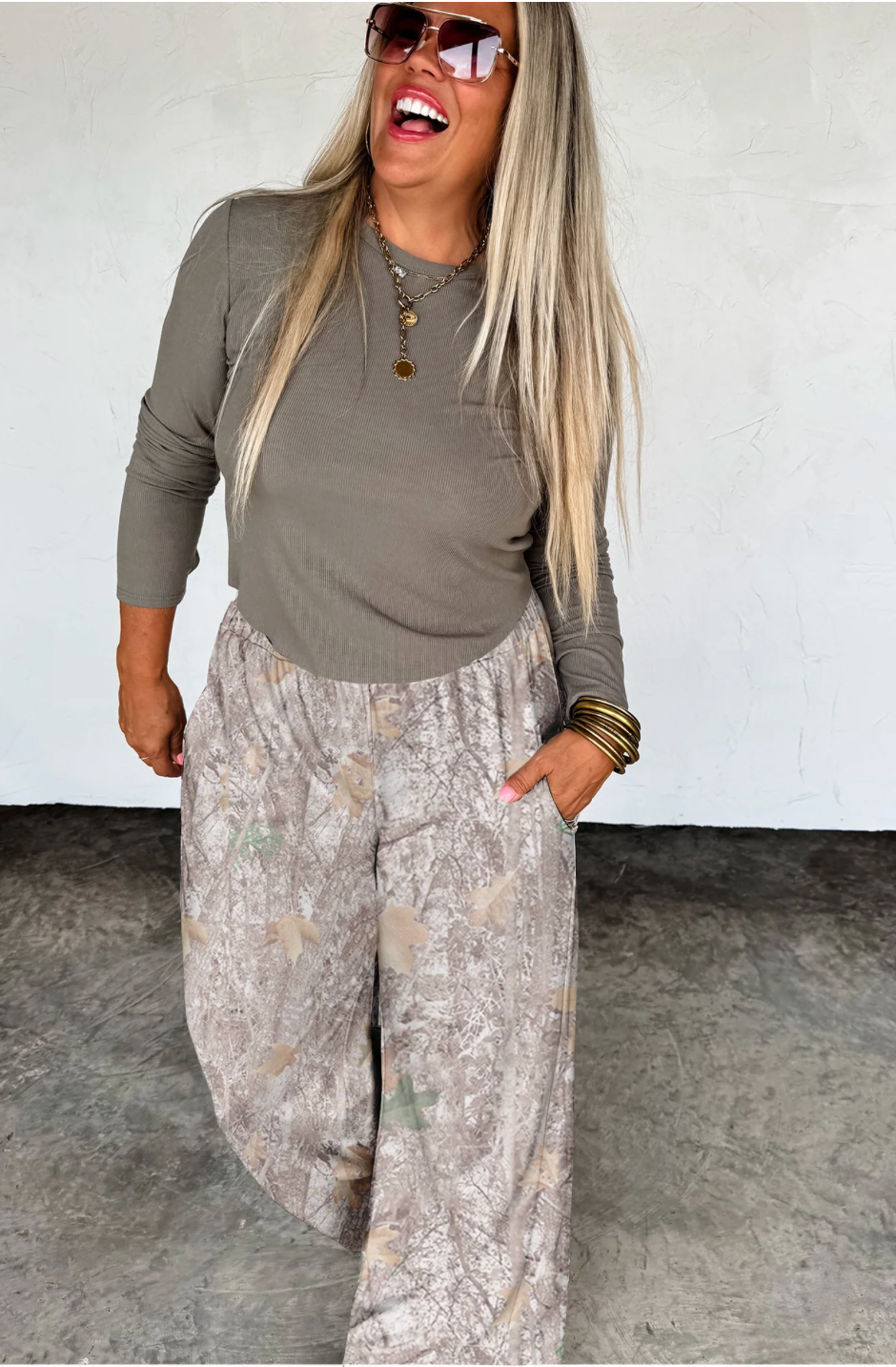 Woman wearing a green top and patterned pants against a white wall.