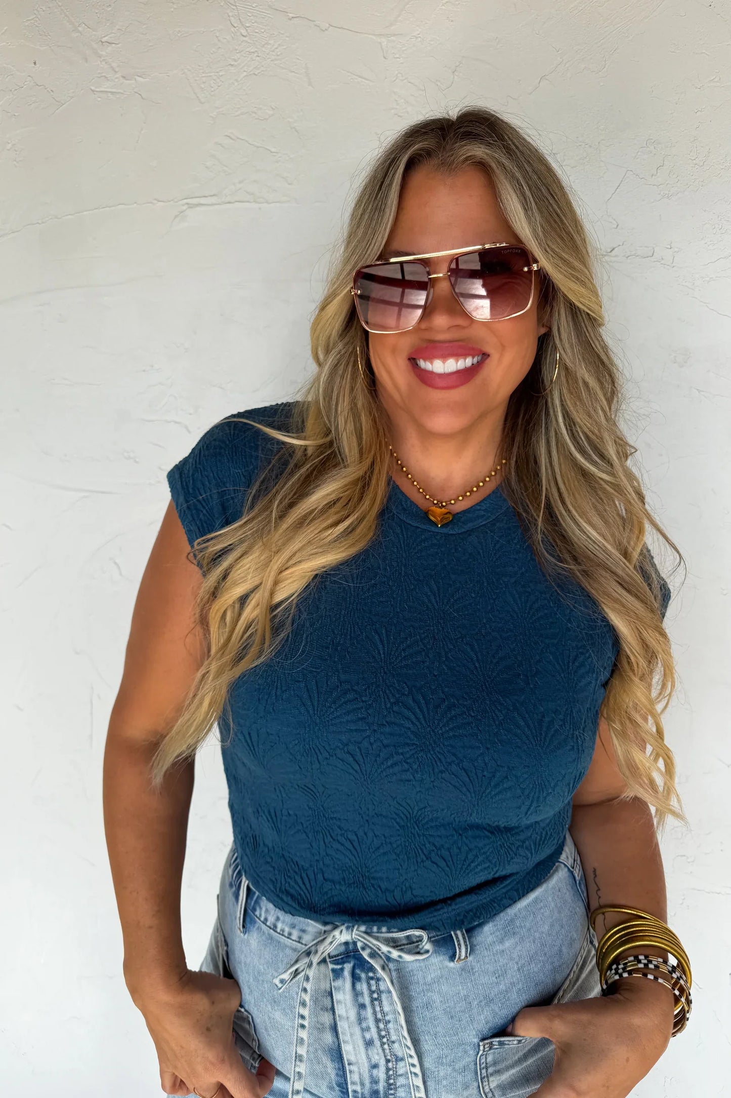 Woman wearing a blue sleeveless top and sunglasses against a white background