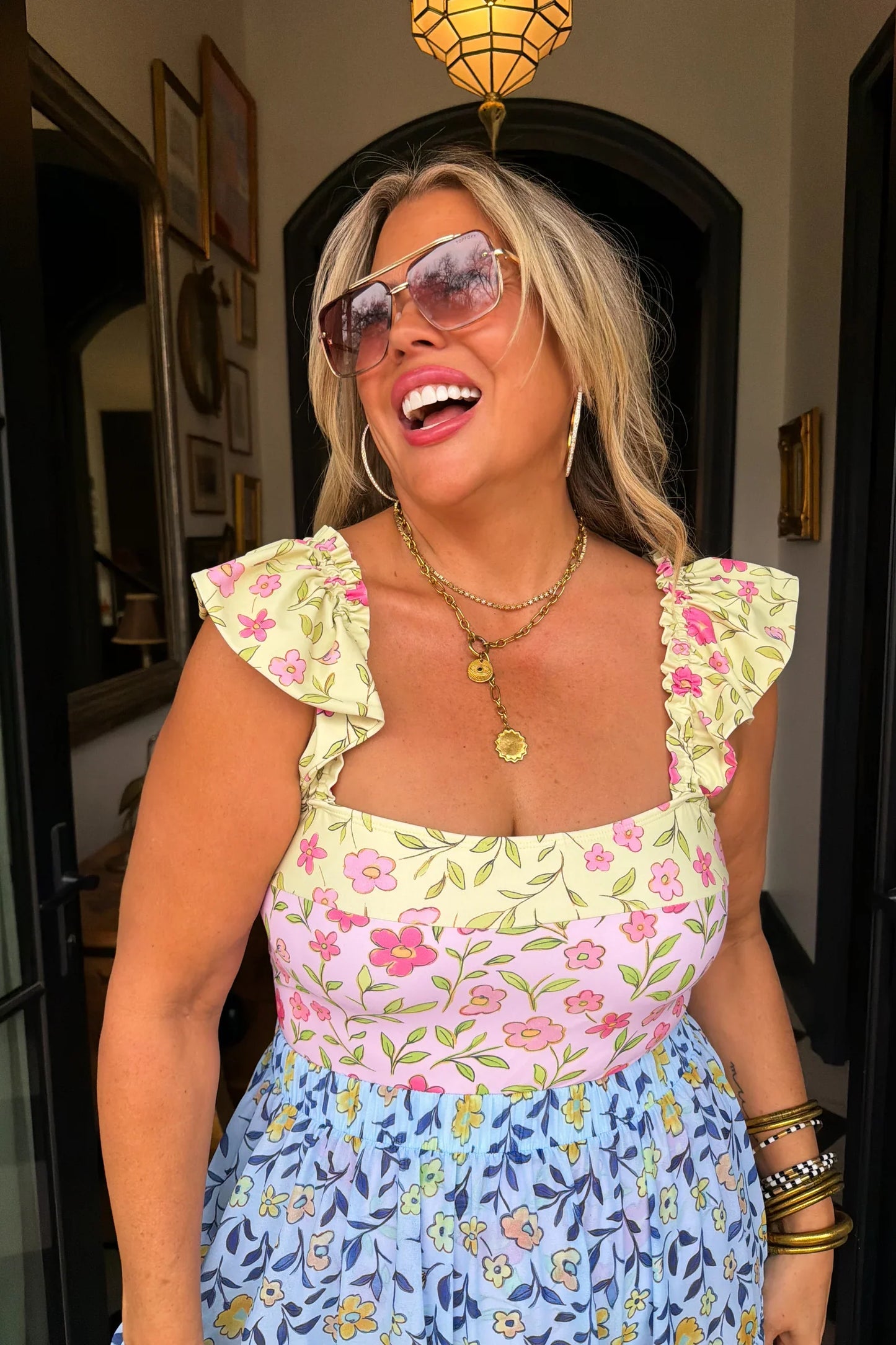 Woman wearing a floral dress with ruffled sleeves and a colorful pattern, standing indoors.