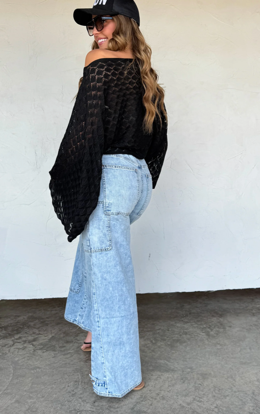 Woman wearing a black top and light blue jeans against a white wall.