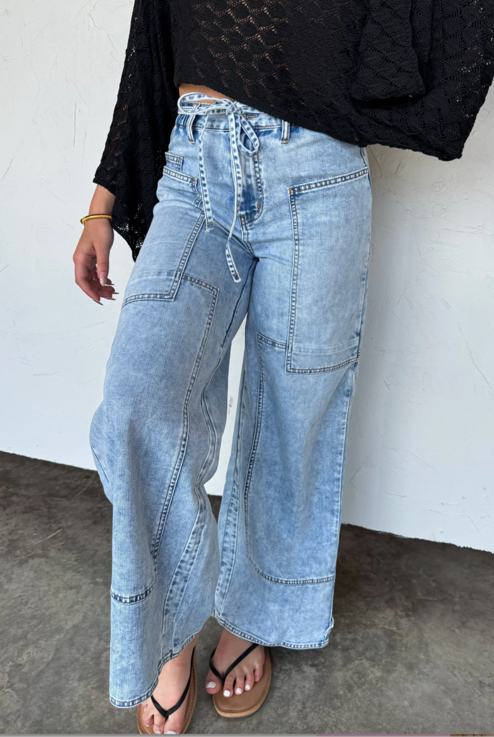 Person wearing light blue wide-leg jeans against a white wall.