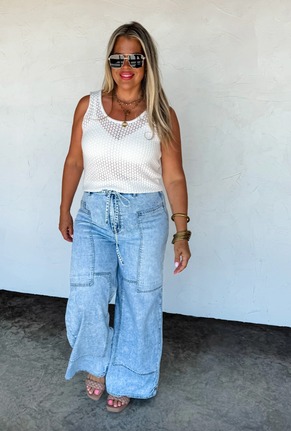 Woman wearing a white sleeveless top and light blue jeans against a white wall.