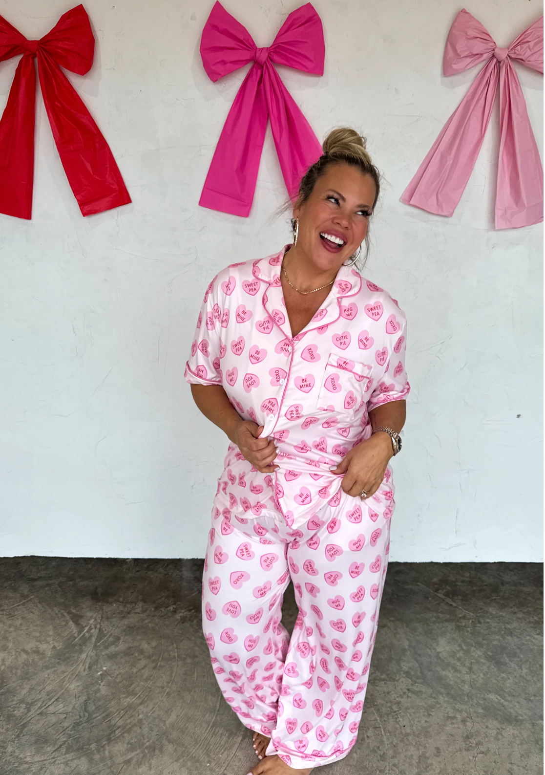 Woman wearing pink pajamas with a floral pattern in front of a white wall with pink bows.