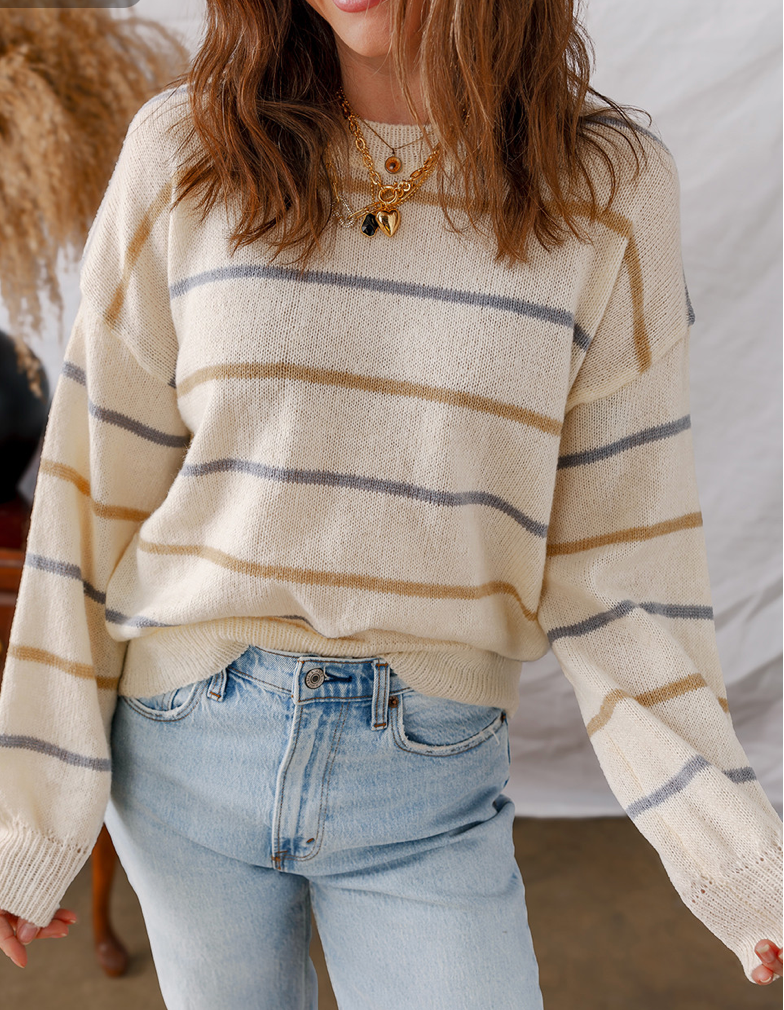 Person wearing a striped sweater and jeans with a neutral background