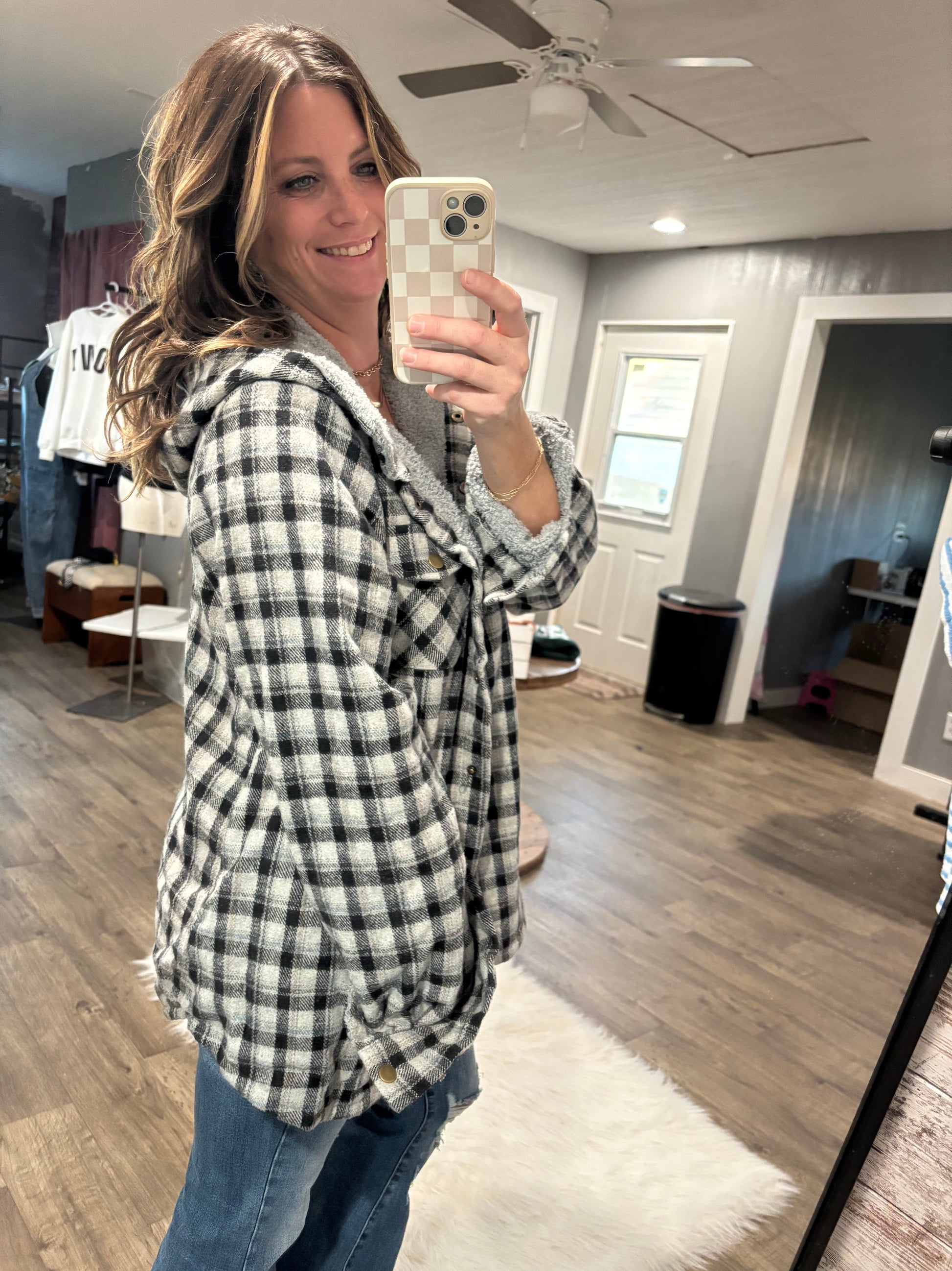 Person wearing a plaid shirt in a room with wooden flooring and a ceiling fan.