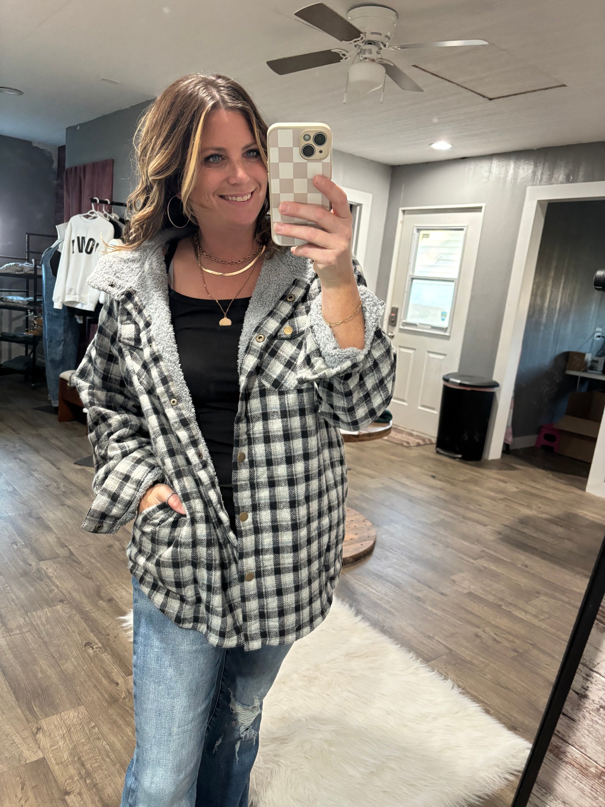 Person wearing a plaid jacket in a room with wooden flooring and a ceiling fan.